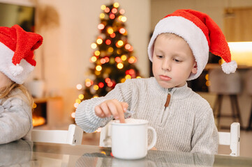 Child drinking from a mug with glowing holiday lights in the background.