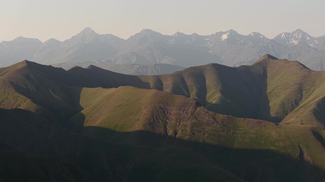 Aerial view of the Alazani pass showcasing rolling green hills meeting rugged mountains in a play of light and shadow, Chala, Tusheti, Georgia.