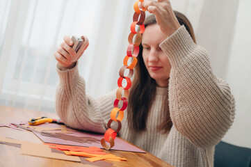 Girl making a paper garland at a table, enjoying creative holiday crafting.