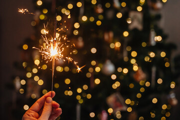 Close-up of sparkler in hand with glowing Christmas tree lights behind