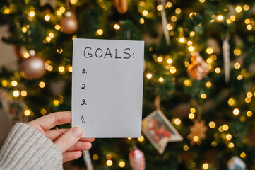 Paper with word GOALS held against glowing Christmas tree lights background