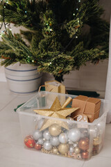 Box of Christmas ornaments next to a small decorated Christmas tree indoors.
