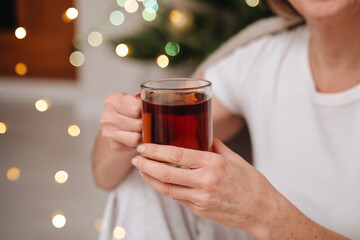 Person holding a clear cup of hot drink with festive Christmas lights in the background