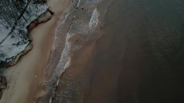 Aerial view of the Baltic sea meeting the shore, showing contrasting textures of the water and the snow covered land, Salacgriva Parish, Limbazi, Latvia.