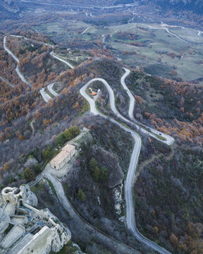 Aerial view of a winding road snaking through the rugged, mountainous terrain, hugging the contours near ancient structures, Pietrapertosa, Basilicata, Italy.