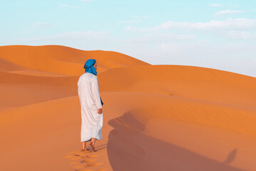 Berber man walking alone on Erg Chebbi dunes at sunset in Merzouga, Sahara Desert, Morocco