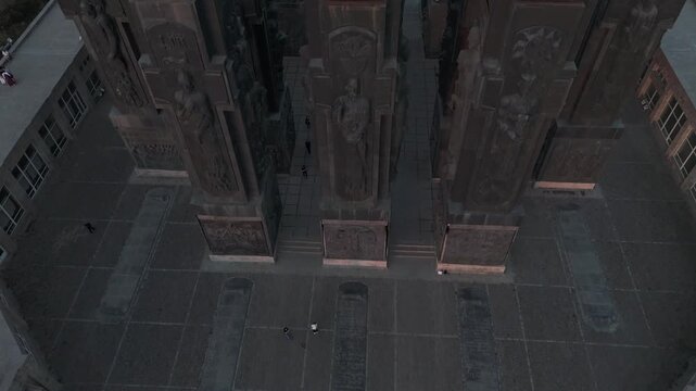 Aerial view of The Chronicle of Georgia's imposing stone pillars with intricate carvings, creating shadows on the paved ground, Tbilisi, Georgia.
