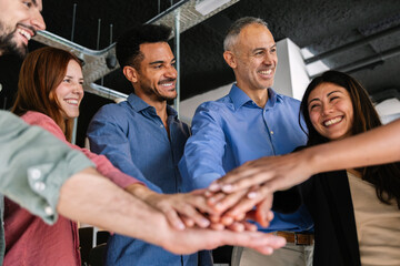 Smiling multiracial business team stacking hands in office symbolizing unity, collaboration, motivation and shared success. Business lifestyle and teamwork concept