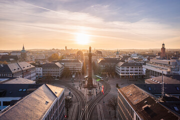 Aerial view of the golden sunlight casting long shadows across Luisenplatz, highlighting the column and tram lines below, Darmstadt, Hessen, Germany.