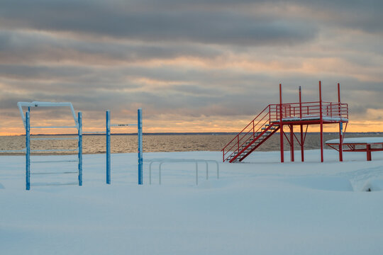 View of the Baltic Sea's frozen shoreline, accented by stark blue and red metal structures against the soft pastel sunset, Parnu, Estonia.