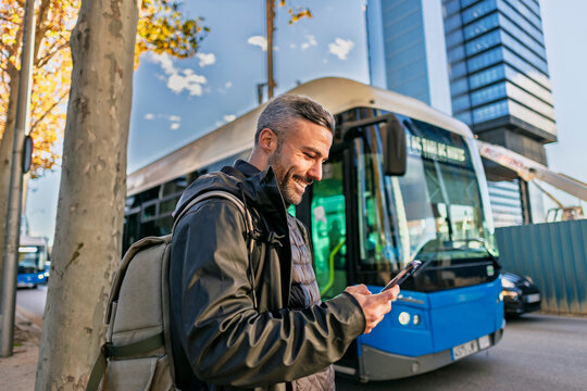 Smiling commuter waiting at bus stop checking phone in urban morning