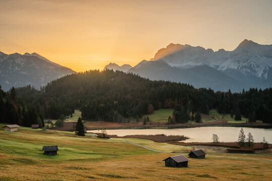 View of golden sunrise painting the rugged mountain peaks and casting a warm glow over the tranquil Geroldsee lake nestled among lush green meadows, Krun, Germany. - Powered by Adobe