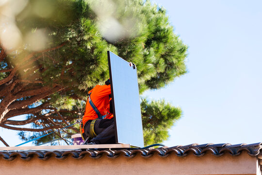 Worker installing solar panel on roof wearing protective gear outdoors