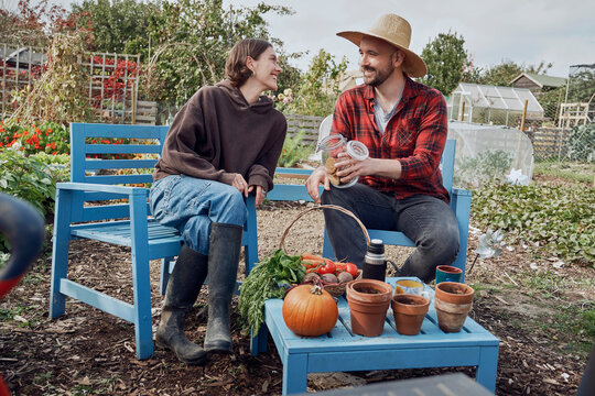 Smiling man and woman sitting in allotment garden with fresh vegetable harvest