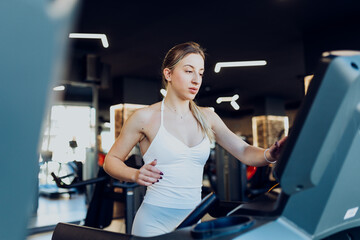 Close-up of a young woman setting up parameters and speed on a digital treadmill console before starting her workout in a modern gym.
