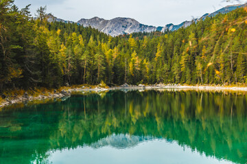 View of emerald waters reflecting the vibrant autumn foliage and towering mountains, creating a serene landscape in Eibsee, Garmisch-Partenkirchen, Bavaria, Germany.