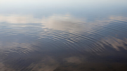 Ripples on calm water surface reflecting sky