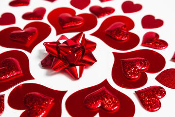 Red metallic gift bow surrounded by shiny hearts on white surface for Valentines Day. Love and celebration decoration concept for holiday design.