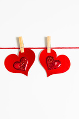 Red glitter heart shapes hanging on a clothesline with clothespin on white background. Love concept for Valentines Day or wedding day.