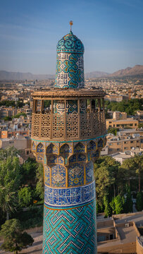 Aerial view of the minaret's intricate turquoise and cobalt tilework glimmers against the warm earth tones of the surrounding city, Isfahan, Giza Governorate, Egypt.