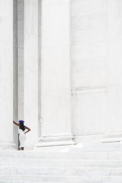 View of a woman stands out in stark contrast against the monumental, white columns, steps, and walls, creating an evocative study in light and shadow, Washington, D.C., District of Columbia, USA.