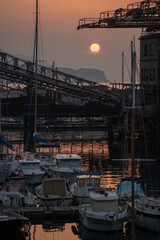 Fototapeta premium Sun rising over bustling harbor with towering cranes and resting ships