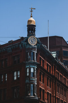 View of a historic brick building adorned with an ornate clock tower crowned with a golden dome and weather vane against a clear blue sky, Washington D.C., District of Columbia, USA.