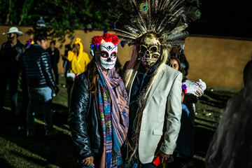 Santa Maria del Tule, Mexico - 03 November 2023: View of two figures adorned in striking Day of the Dead attire, masks gleaming amidst the shadows of the Day of the Death cementary.