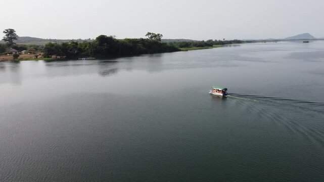 Aerial drone footage of Ghana, Africa, serene lake surrounded by mountains. Traditional boats across the water near a local village, with views near the Right to Dream Football Academy