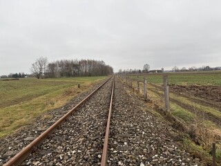 Fototapeta premium Old and degraded railway line before modernization, with rusty rails and worn wooden sleepers. Abandoned and neglected tracks stretching into the distance, symbolizing decay.