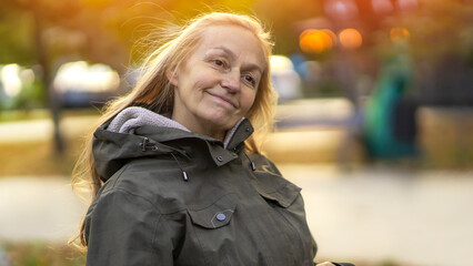 Fototapeta premium Old cheerful woman with a smiiley face walks in the city in the autumn sunny day.