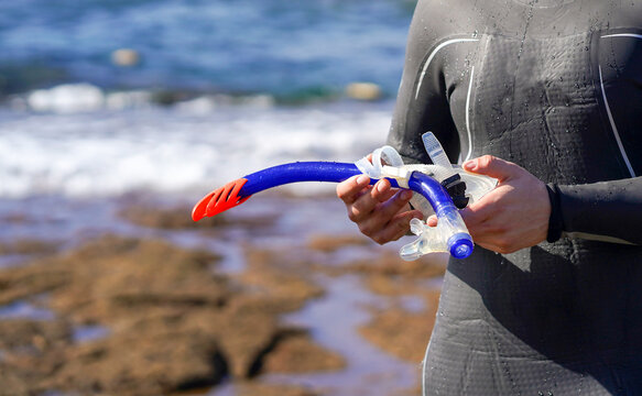 A man holds a mask and snorkeling tube for swimming in the ocean on a sunny day.