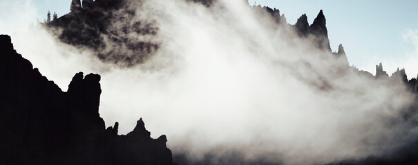 A mysterious landcape with dark silhouettes of rocky mountains in a fog.