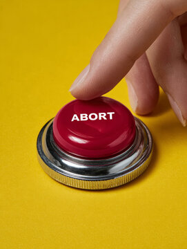 Hand pressing a red abort button on yellow background.