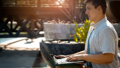 A man is sitting in a park and working on a laptop outdoors.