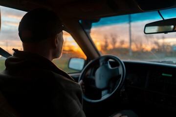 A man is driving his car on the road at sunset.