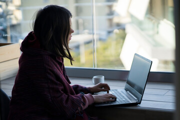 Girl is working at a laptop, typing on a keyboard indoors.