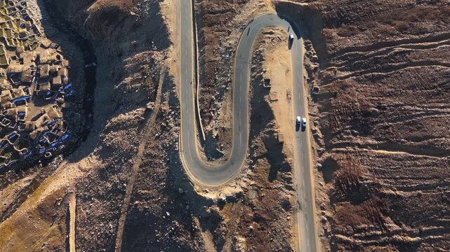 Aerial view of a winding road with cars cutting through the rugged terrain, creating a stark contrast to the arid landscape, Gittidas, Khyber Pakhtunkhwa, Pakistan.