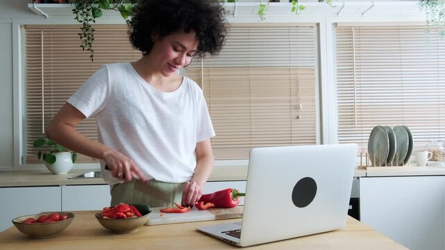Young woman following an online recipe on a laptop and cooking