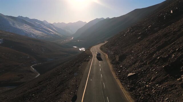 Aerial view of a vehicle on the winding road surrounded by rugged mountains and valleys, showcasing a blend of light and shadows, Babusar Pass, Khyber Pakhtunkhwa, Pakistan.