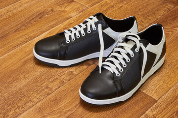 a pair of new sneakers lying on brown laminate, black and white sneakers for everyday wear on a wooden background