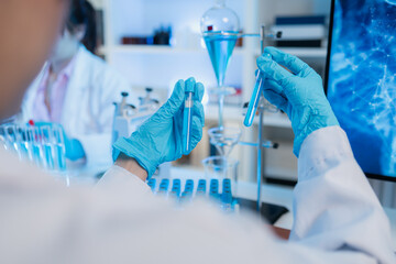 Two female scientists in white lab coats working together in a bright laboratory with microscopes, glassware, and blue test tubes, representing teamwork and modern scientific research environment.