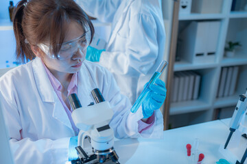 Two female scientists in white lab coats working together in a bright laboratory with microscopes, glassware, and blue test tubes, representing teamwork and modern scientific research environment.