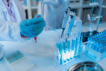 Two female scientists in white lab coats working together in a bright laboratory with microscopes, glassware, and blue test tubes, representing teamwork and modern scientific research environment.