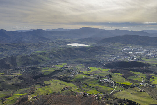 Aerial view of rolling hills punctuated by verdant fields and distant mountains fading into the horizon, with a serene lake mirroring the sky, Potenza, Basilicata, Italy.