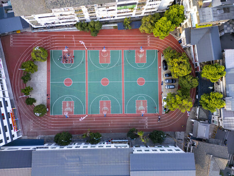 Aerial view of vibrant green basketball courts nestled amidst a red running track and bordered by buildings and lush trees, Yangshuo, Guangxi, China.