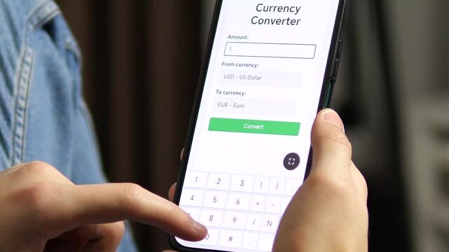 This closeup shows a person preparing to convert Euros to US Dollars in a currency converter app, inputting the amount and selecting currencies. It embodies international finance, travel preparation