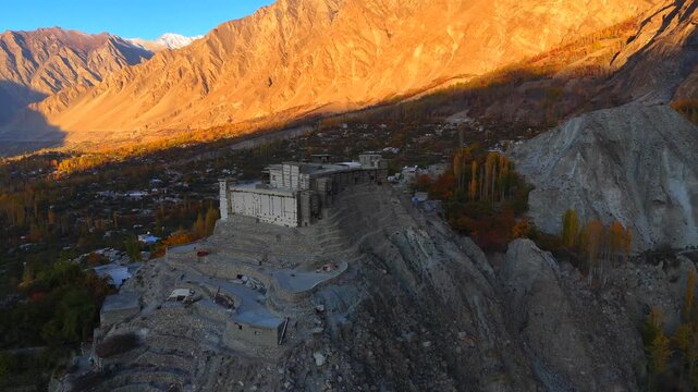 Aerial view of the Baltit Fort on a rocky hill, with the golden light on the mountains in the background, Karimabad, Gilgit Baltistan, Pakistan.
