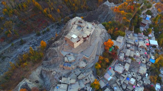 Aerial view of Baltit Fort sitting atop a craggy hill surrounded by autumn foliage and clustered homes with flat roofs, Karimabad, Gilgit Baltistan, Pakistan.