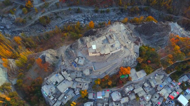 Aerial view of Baltit Fort, a historic structure atop a hill, surrounded by vibrant autumn foliage and a village with gray rooftops, Karimabad, Gilgit Baltistan, Pakistan.